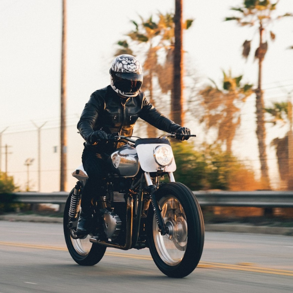 Person riding a motorcycle wearing an earpeace earplug on a road with palm trees in the background
