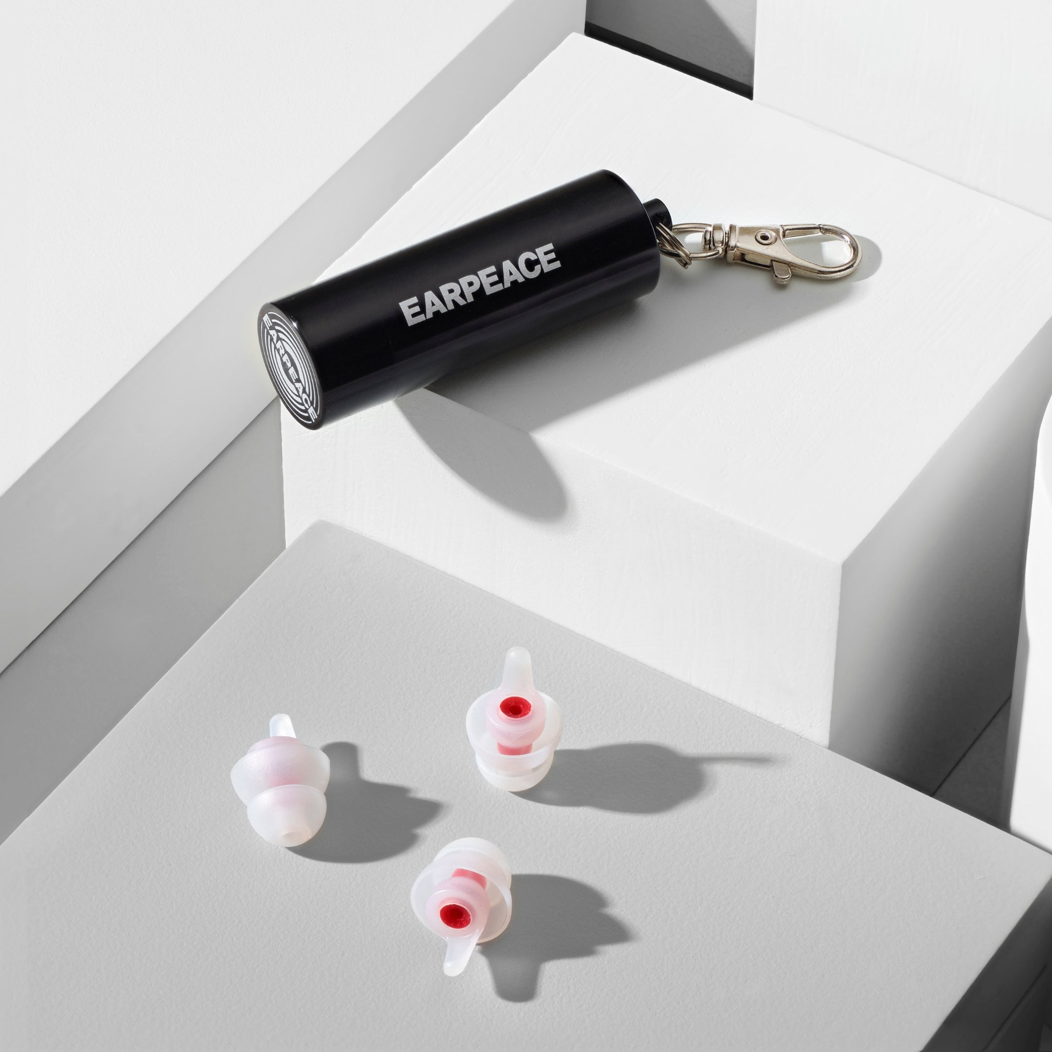 Black 'EARPEACE' container with earplugs on a white surface